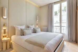 Quarto moderno com uma cama grande, mesas de cabeceira, arandelas e vista para o exterior.