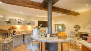 Una cucina moderna con isola in pietra, un tavolo da pranzo centrale con sedie, un camino in pietra e un ampio camino.