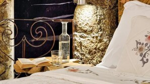 Una stanza con parete in pietra, una scala a chiocciola in metallo, un vaso grande, un letto con biancheria da letto floreale e un tavolino con un libro e dei bicchieri.