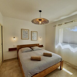 Ein Schlafzimmer mit einem hölzernen Bett, einer gewobenen Deckenleuchte, Wandbildern und einem Fenster mit Blick.