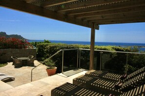 Eine Terrasse im Freien mit Meerblick, einer Pergola, Korbmöbeln und einem Blumentopf.