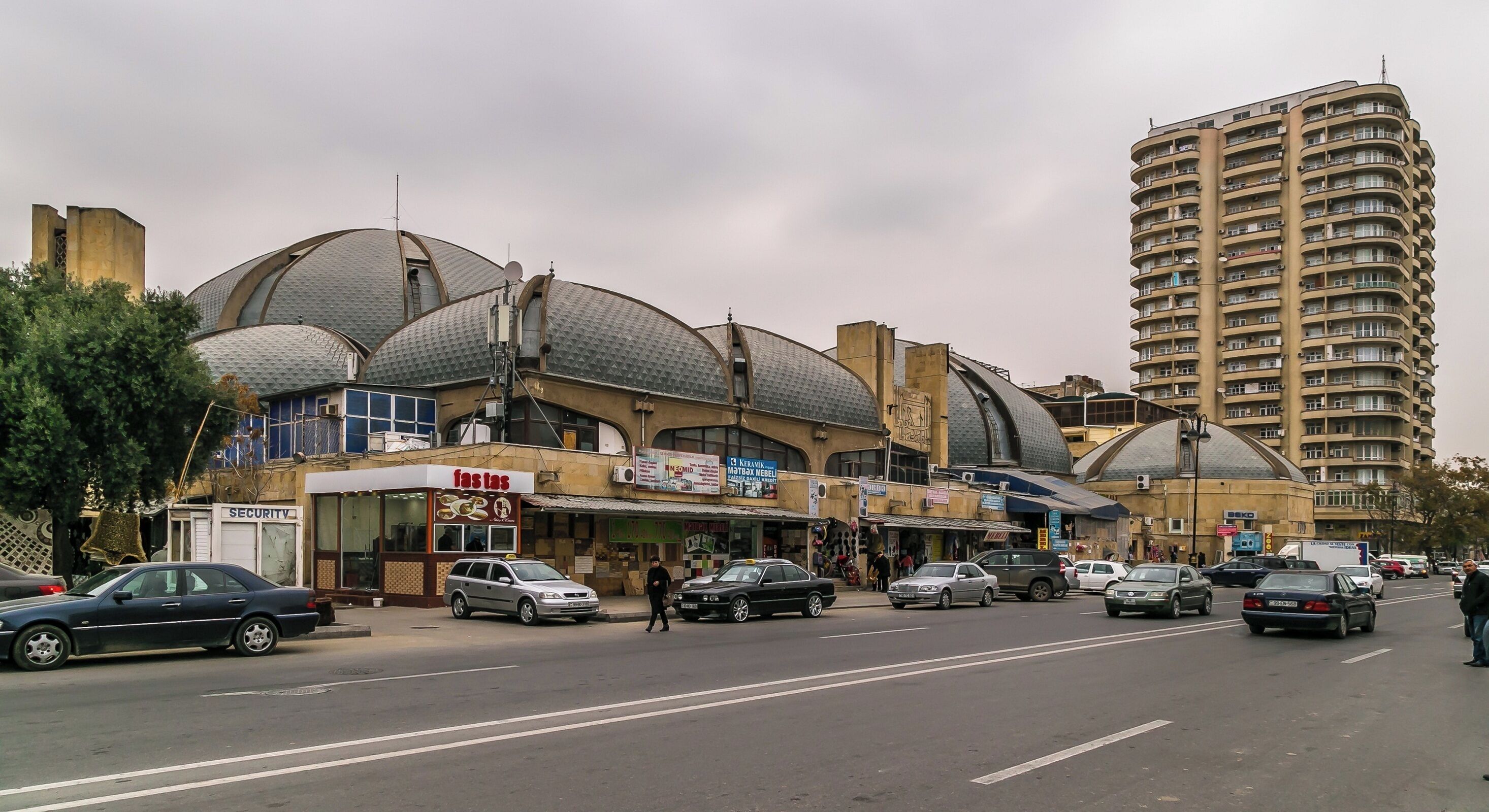 A street with a large building featuring multiple domed structures and a tall residential building in the background.
