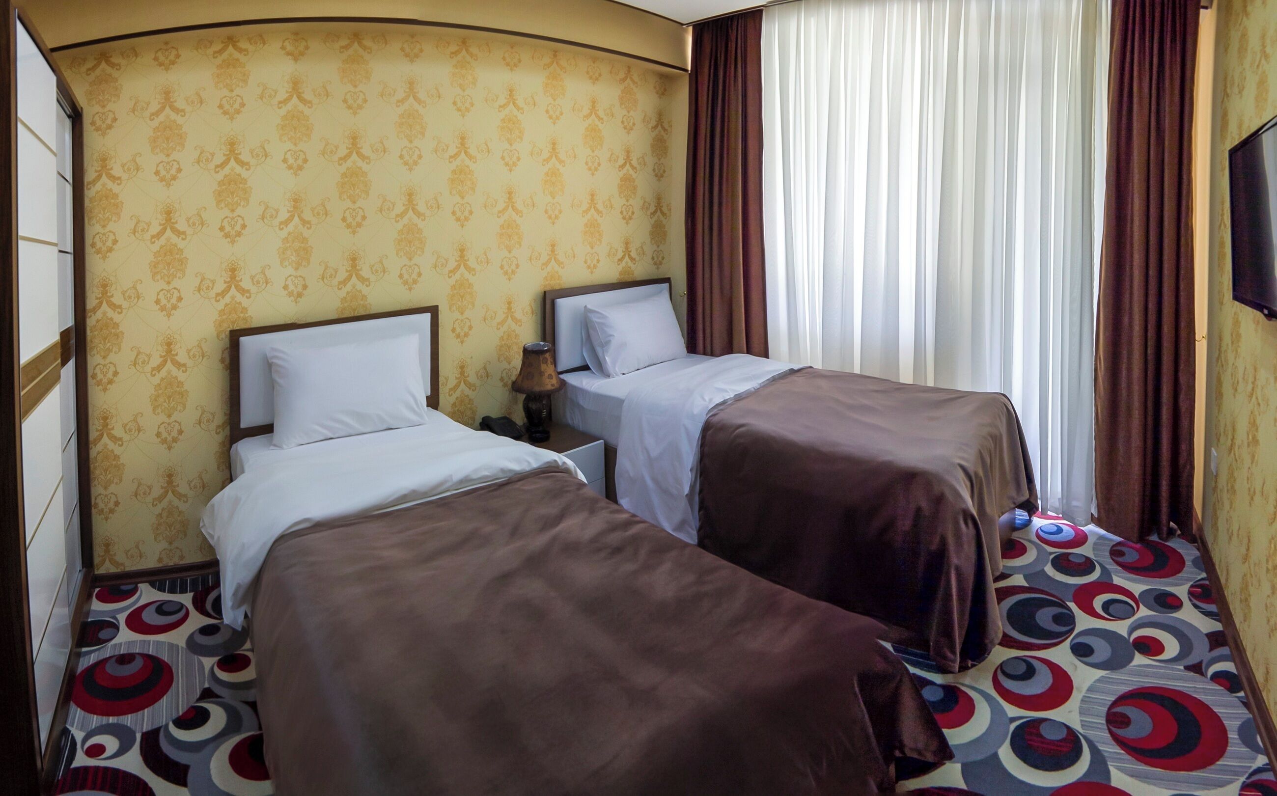 Ein Hotelzimmer mit zwei Betten, einer strukturierten Wand, Vorhängen und einem Fernseher.