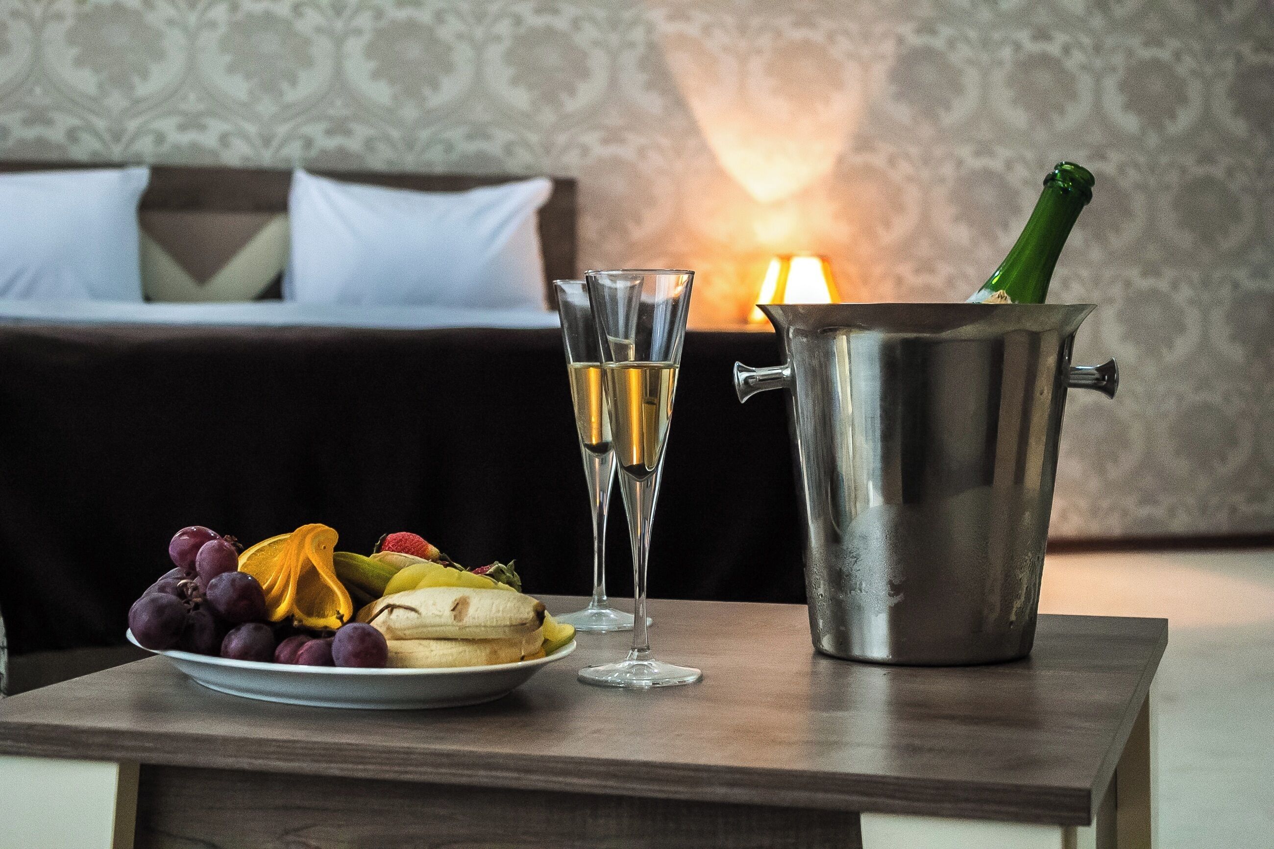 Et bord med et fad med frugt, to champagneglas og en champagneflaske i en metalspand.