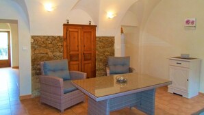 Una habitación con pared de piedra, armario de madera, sillas de mimbre, una mesa de vidrio y un mueble blanco.