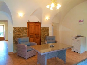 Ein Zimmer mit Steinwand, Holzschrank, Korbstühlen, einem Glastisch und einem weißen Schrank.