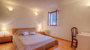 Un dormitorio con cama, lámparas de noche, una silla, un escritorio, una ventana y un radiador.
