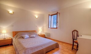 Ein Schlafzimmer mit Bett, Nachttischlampen, einem Sessel, einem Schreibtisch, einem Fenster und einer Heizung.