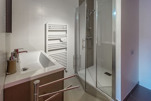 A modern bathroom with a glass shower enclosure, a white sink, and a towel rack.