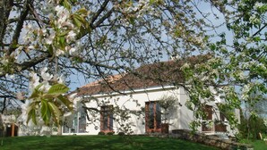 A white building with a tiled roof, surrounded by a well-maintained lawn and flowering trees. - Guest Room “La Grange Fleurie” with Shared Terrace, Garden, and Wi-Fi (Rochechouart)