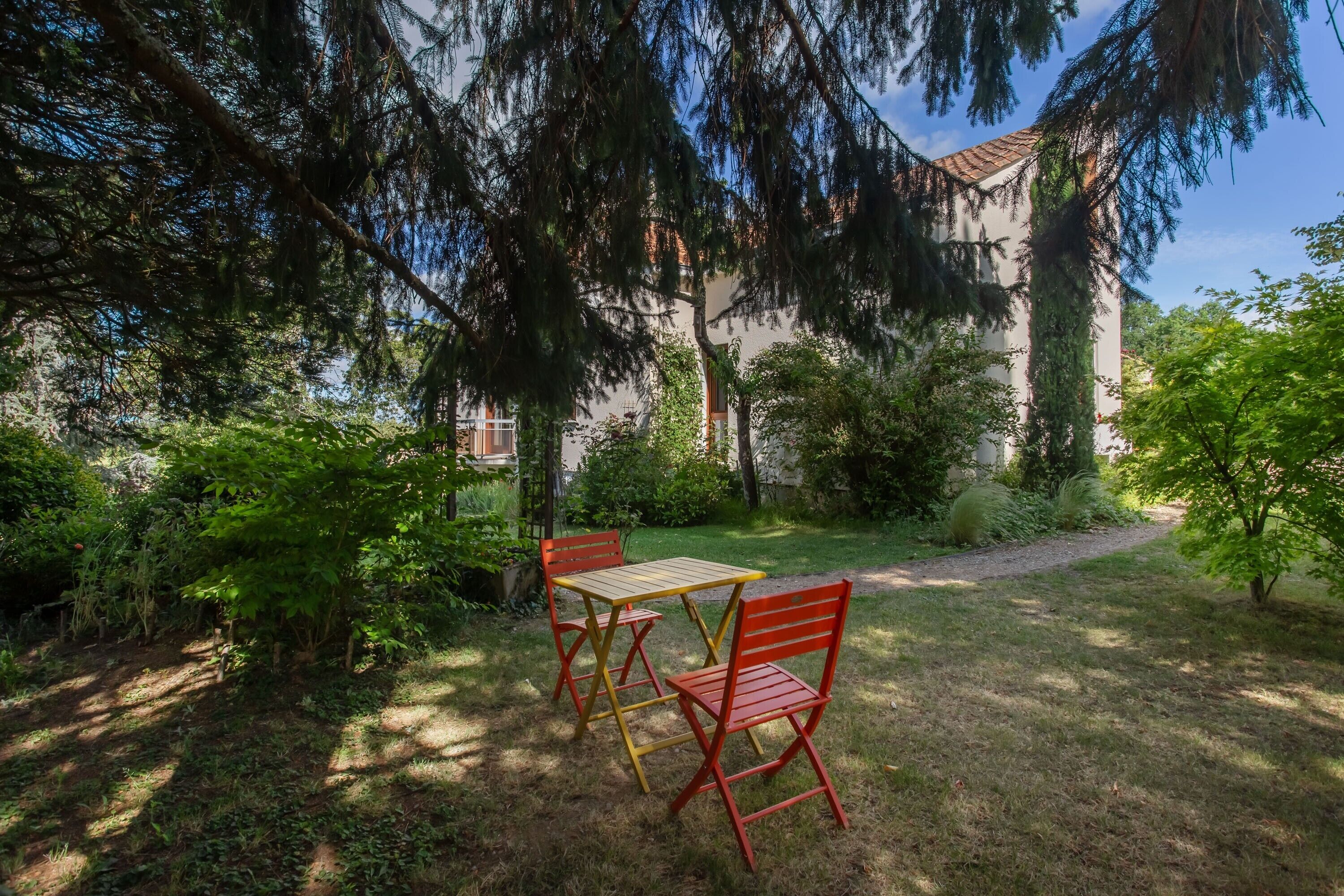 A garden with a table and chairs, surrounded by greenery and a building in the background.