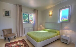 Ein Schlafzimmer mit Bett, Sessel, Nachttisch, Lampe, Fenster und Heizkörper.