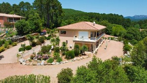Une maison à deux étages dotée d’un balcon, entourée d’un jardin aménagé avec différentes espèces de plantes et disposant d’une allée.