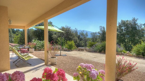 Un espace extérieur abrité, équipé d’une table et de chaises, d’une plante en pot, et offrant une vue sur un paysage montagneux.