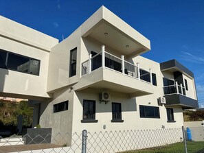 A modern multi-story building with balconies, large windows, and a chain-link fence.