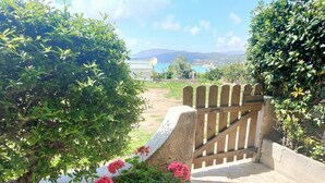 Un jardín con muro de piedra, portón de madera y flores rosadas.