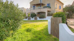 Una casa de dos pisos con un balcón, un pequeño jardín y una valla de madera.