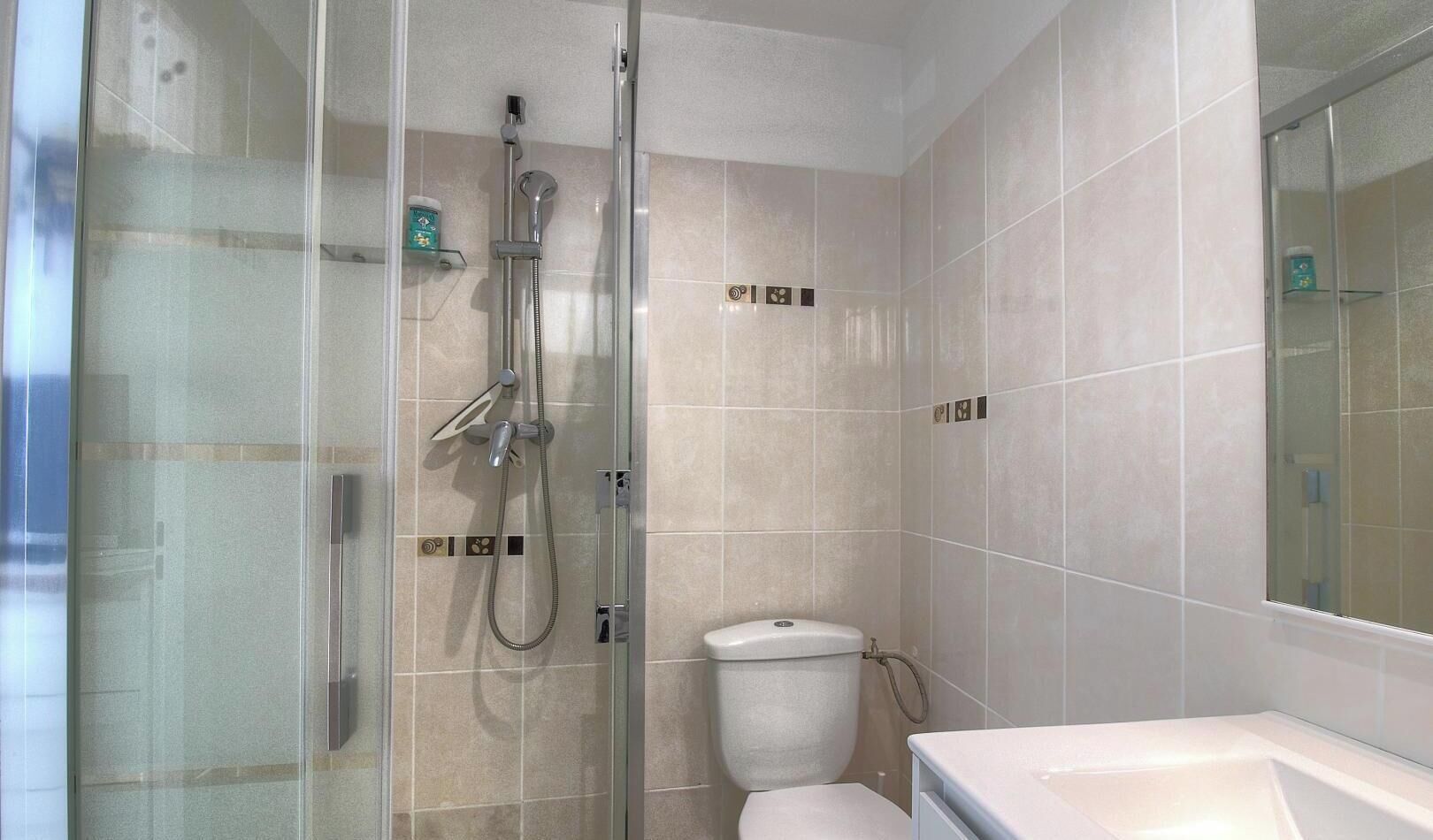 A bathroom with a glass shower enclosure, a toilet, and a sink.