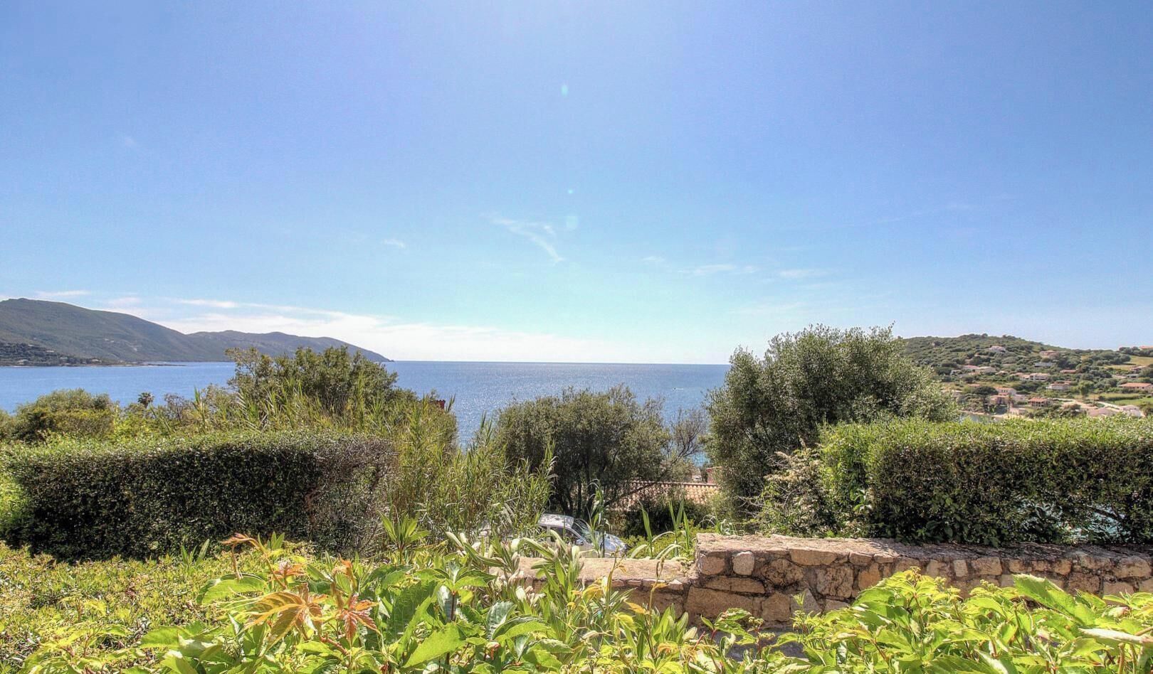 Paisagem costeira com vista para o mar, vegetação e colinas ao longe.