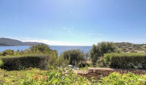 Eine Küstenlandschaft mit Blick auf das Meer, viel Grün und ferne Hügel.