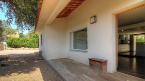 Una casa moderna con terraza de madera, un ventanal grande y una cocina visible a través de una puerta abierta.