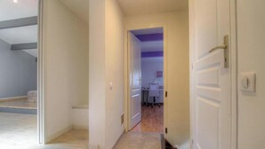 Un pasillo que conduce a una habitación con una puerta, un baño visible y un techo con vigas a la vista.
