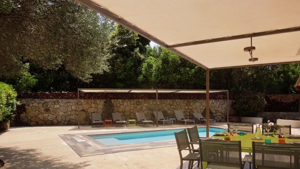 Zona de piscina exterior con sillones de descanso y una mesa de comedor bajo una pérgola.