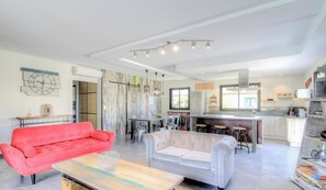 Ein modernes Wohnzimmer mit einem roten Sofa, einem weißen Sofa und einem Couchtisch aus Holz. Es gibt eine Küchenzeile mit einer Bar und Hockern.