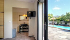 Ein Badezimmer mit Waschbecken, Spiegel und Fernseher, das in einen Poolbereich mit Liegestühlen führt.