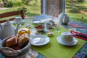 A breakfast table set with white teapots, cups, a bowl of strawberries, bread, and a green placemat.