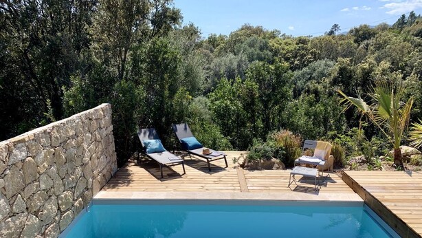 Una piscina con sillas de descanso y un muro de piedra.