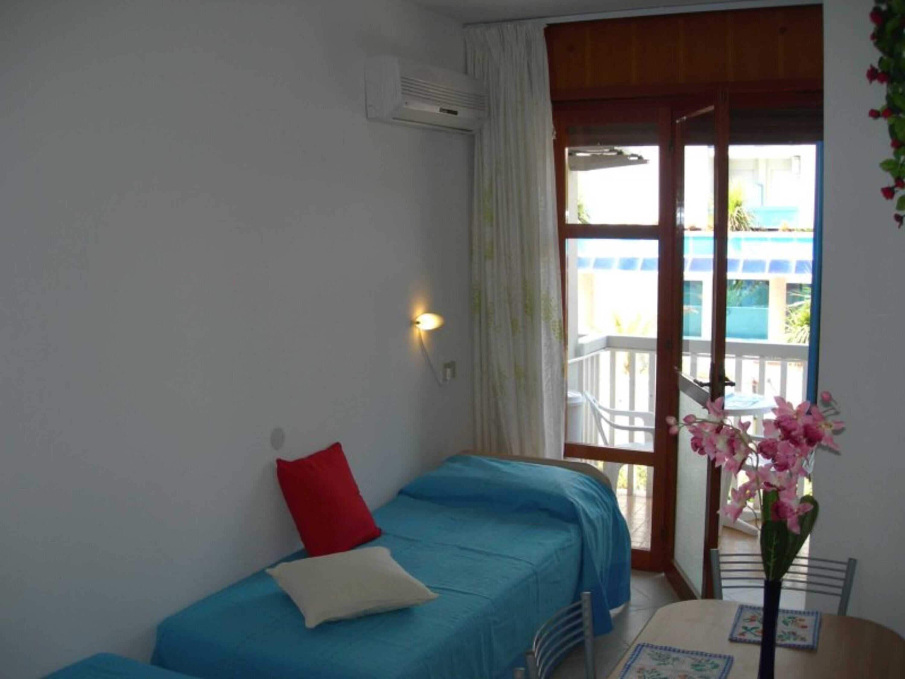 A room with two beds, a table with a vase of flowers, and a balcony with a view.