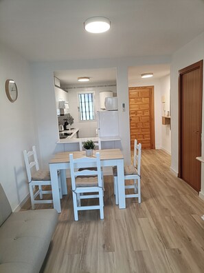 A modern kitchen with white appliances, a dining table with chairs, and a wooden door. - Apartment at the foot of Sierra de Irta, Hiking, Nature, Mountain and Sea. (Peñíscola)