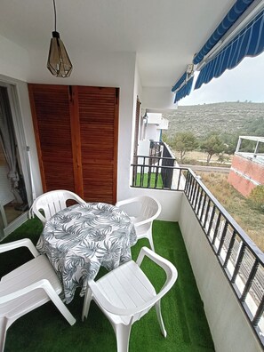 Ein Balkon mit Tisch und Stühlen, einer hängenden Leuchte und Blick auf eine hügelige Landschaft.