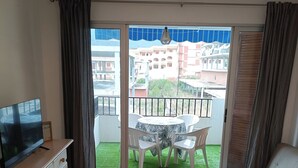 Een woonkamer met een televisie, een bank, een eettafel en een balkon met uitzicht op gebouwen.