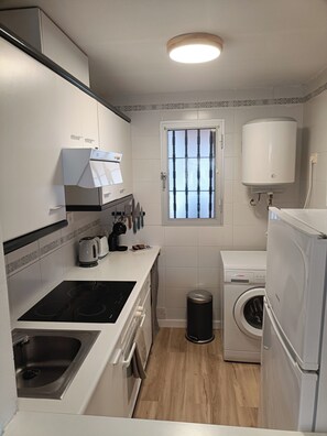 A compact kitchen with a built-in stove, a sink, a window, a washing machine, and a water heater. - Apartment at the foot of Sierra de Irta, Hiking, Nature, Mountain and Sea. (Peñíscola)