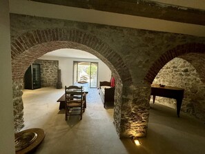 Ein rustikales Interieur mit Steinbögen, einem Esstisch und einem Kamin.