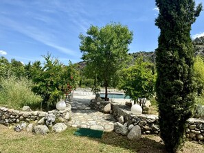 Ein steinbelagter Weg führt zu einem Pool, der von Bäumen umgeben ist, mit einem Bergpanorama im Hintergrund.