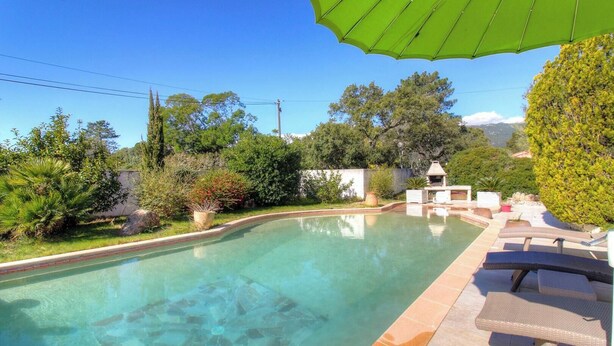 Una piscina con borde de azulejos, rodeada de vegetación y una zona de barbacoa.