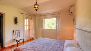 Un dormitorio con una cama, una silla, una lámpara colgante y una ventana.
