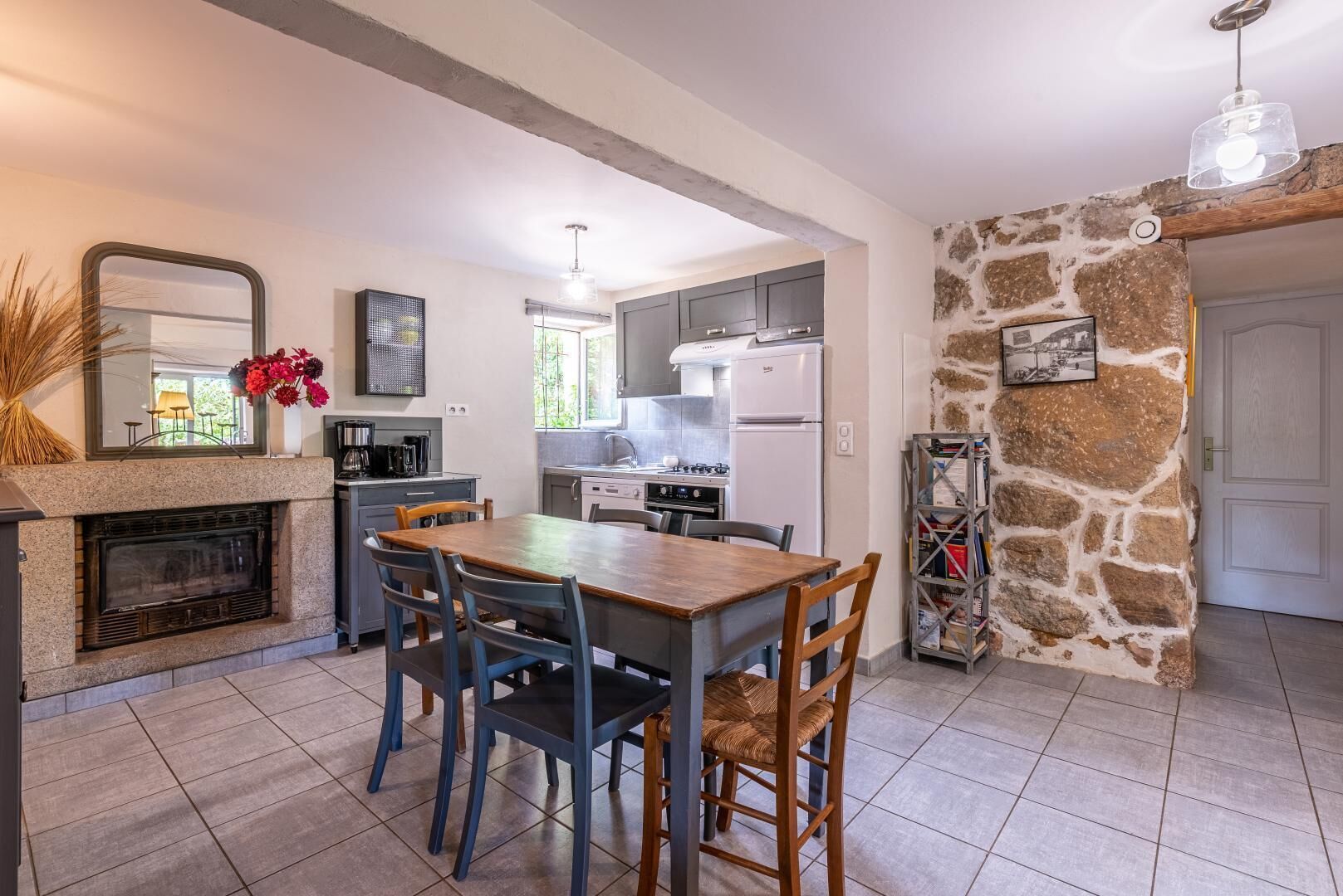 A kitchen with a stone wall, a fireplace, and a dining area with chairs.