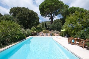 Ein Swimmingpool mit Liegestühlen und einem Tisch, umgeben von viel Grün und Bäumen.