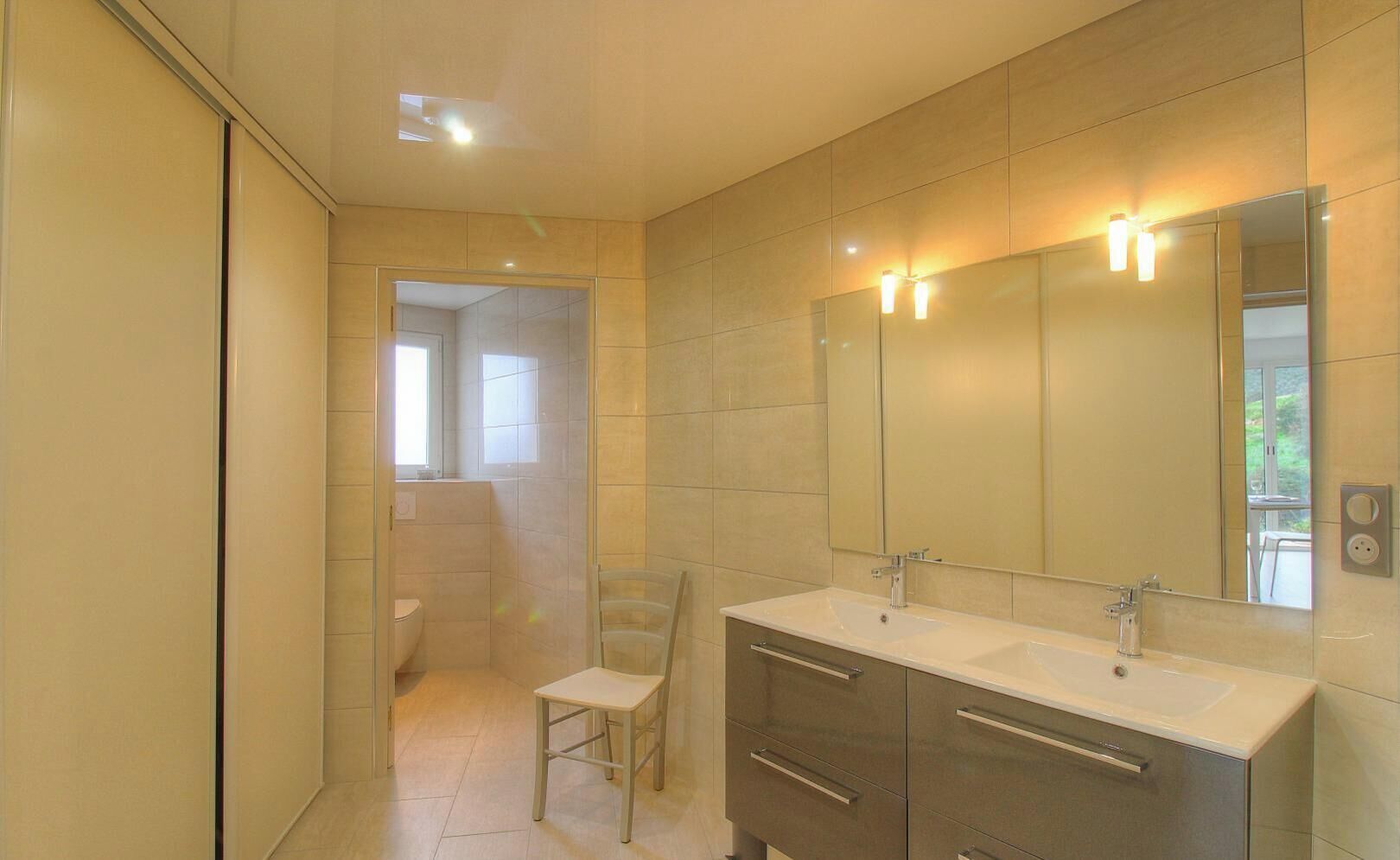 Une salle de bain moderne équipée d’une douche, de toilettes, d’un lavabo avec un grand miroir et d’une chaise.