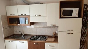 A compact kitchen with a sink, stove, microwave, and cabinets. - Sea view flat in Bibione for four guests (Bibione)