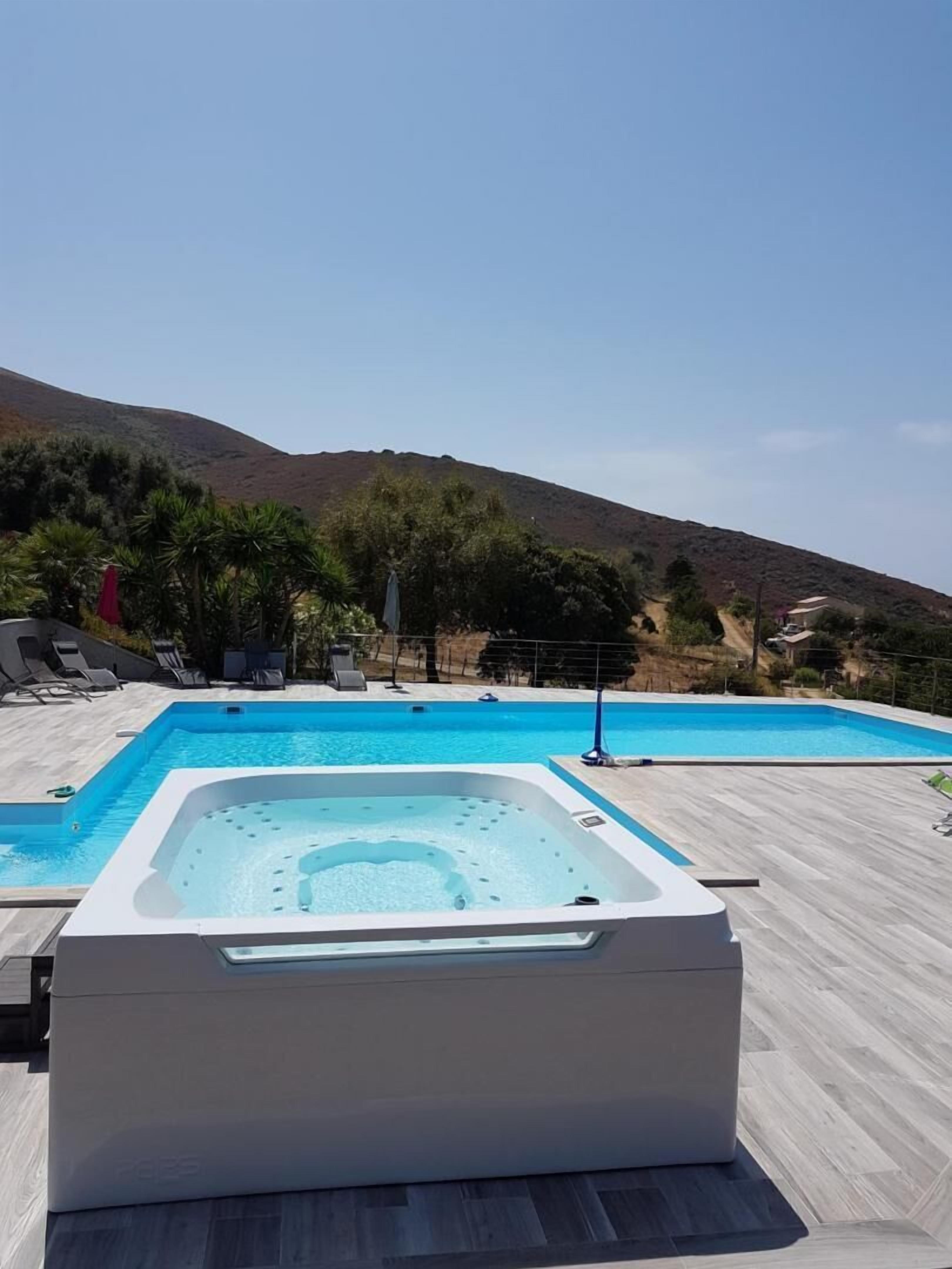 A swimming pool with a hot tub, lounge chairs, and a mountainous backdrop.