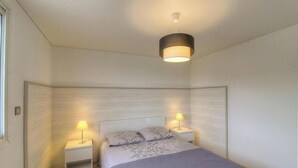 Un dormitorio con cama, dos mesitas de noche, lámpara colgante y ventana.