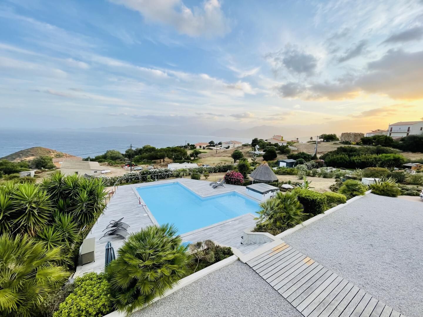 A swimming pool with a view of the sea, surrounded by greenery and buildings.