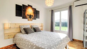 A bedroom with a wooden headboard, a bed with patterned bedding, a wall-mounted artwork, a ceiling light fixture, and a window with curtains. - In the Meadow of the Kites - CUTTOLI CORTICCHIATO (CUTTOLI CORTICCHIATO)