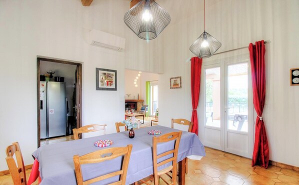 Un coin repas avec une table dressée pour six personnes, des chaises en bois, un lustre et une vue sur la cuisine et l’extérieur.