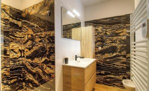 Ein Badezimmer mit Marmorwand, Waschbecken, Spiegel und Toilette.